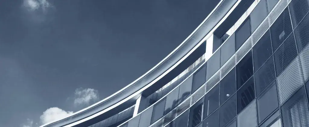 La façade incurvée d'un bâtiment moderne en verre et en acier se détache sur un ciel bleu clair, reflétant la stabilité, tout comme le choix d'un contrat électricité prix fixe pour la tranquillité d'esprit.