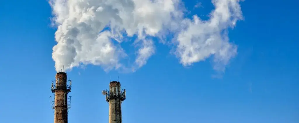 Deux cheminées industrielles émettent de la fumée blanche dans un ciel bleu clair