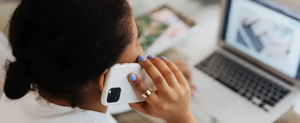 Personne tenant un smartphone à l'oreille et regardant l'écran d'un ordinateur portable, entourée de documents et d'un carnet de notes - peut-être en train de réviser sa stratégie d'achat d'énergie.