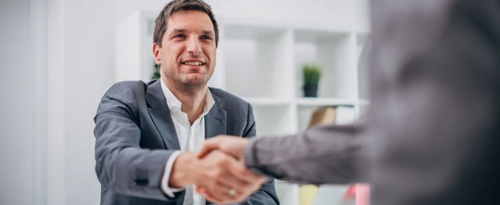 Un homme en costume est assis à un bureau, souriant et serrant la main d'une autre personne dans un bureau ENGIE.
