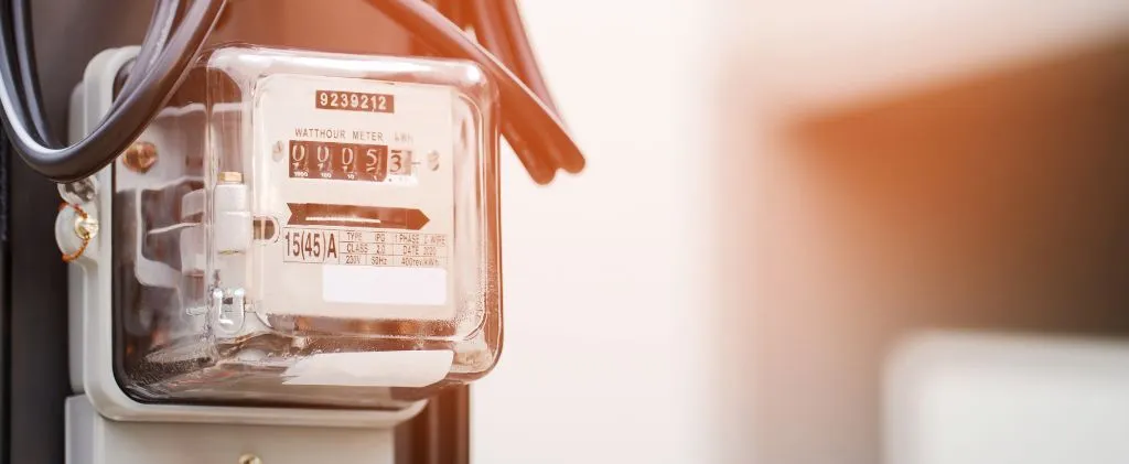 Gros plan d'un compteur électrique analogique Linky monté sur un mur, affichant son relevé à travers un couvercle transparent auquel sont attachés des fils visibles.