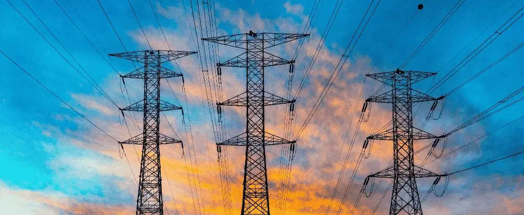 Trois pylônes de transmission électrique avec des lignes électriques se détachent sur un ciel coloré avec des nuages, symbolisant le flux d'énergie qui a un impact sur chaque tarif electricite professionnel.