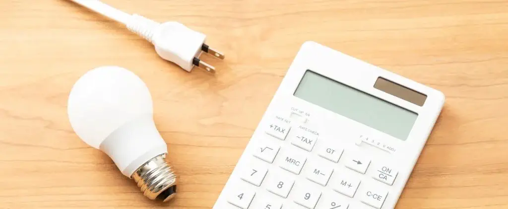 Une calculatrice blanche, une ampoule et un cordon d'alimentation sont posés sur une surface en bois, symbolisant les inquiétudes quant à l'avenir hausse ticgn ticfe 2026.